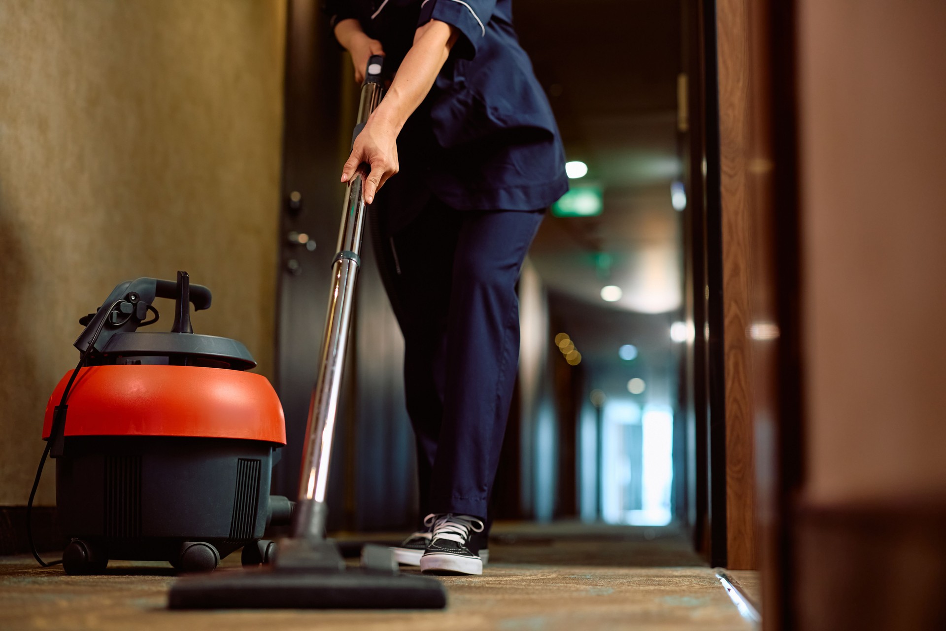 Close up of woman vacuuming hallway while working as maid in a hotel.